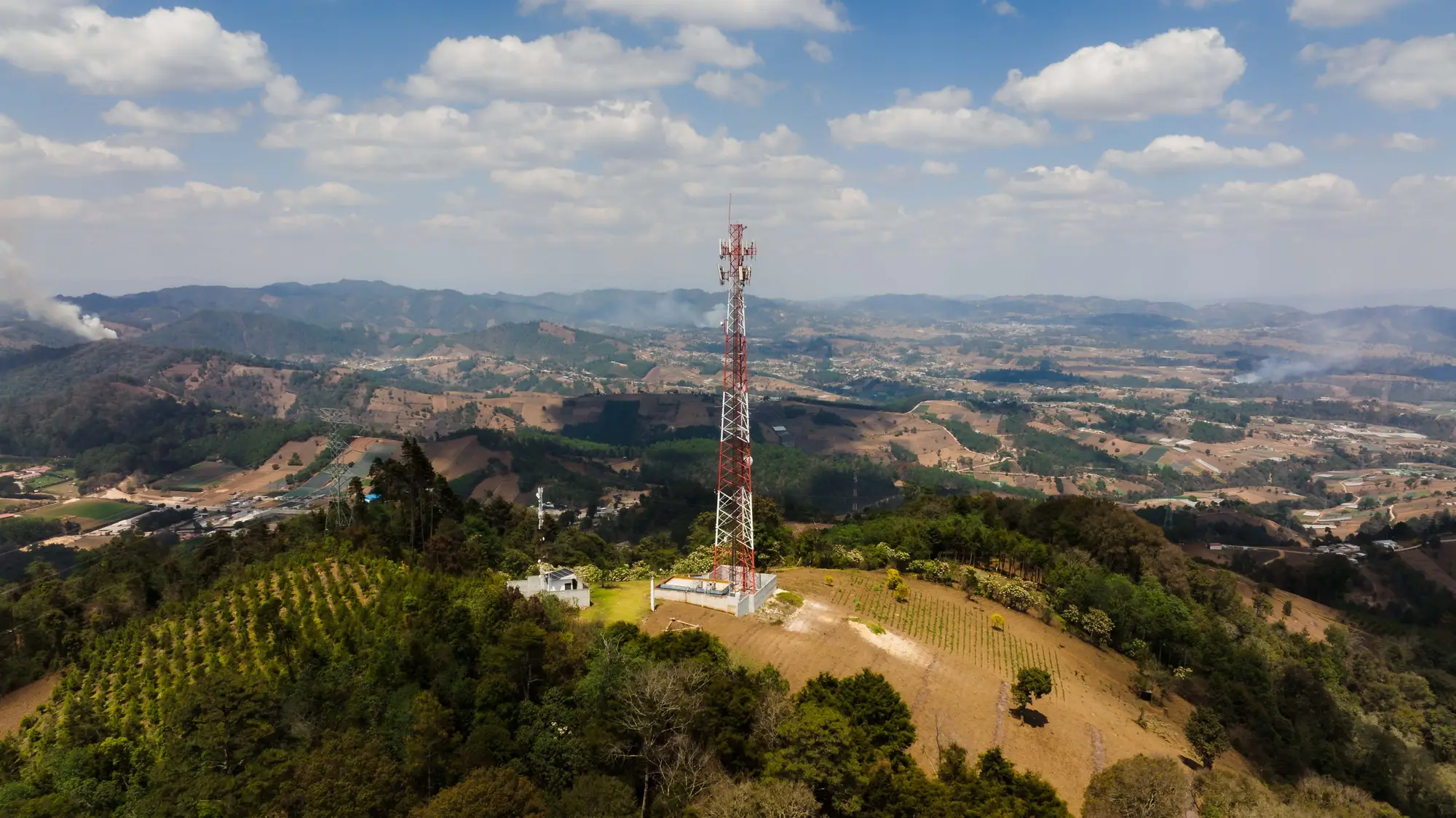 A lattice mast on a hilltop above rolling farmland and distant ridges